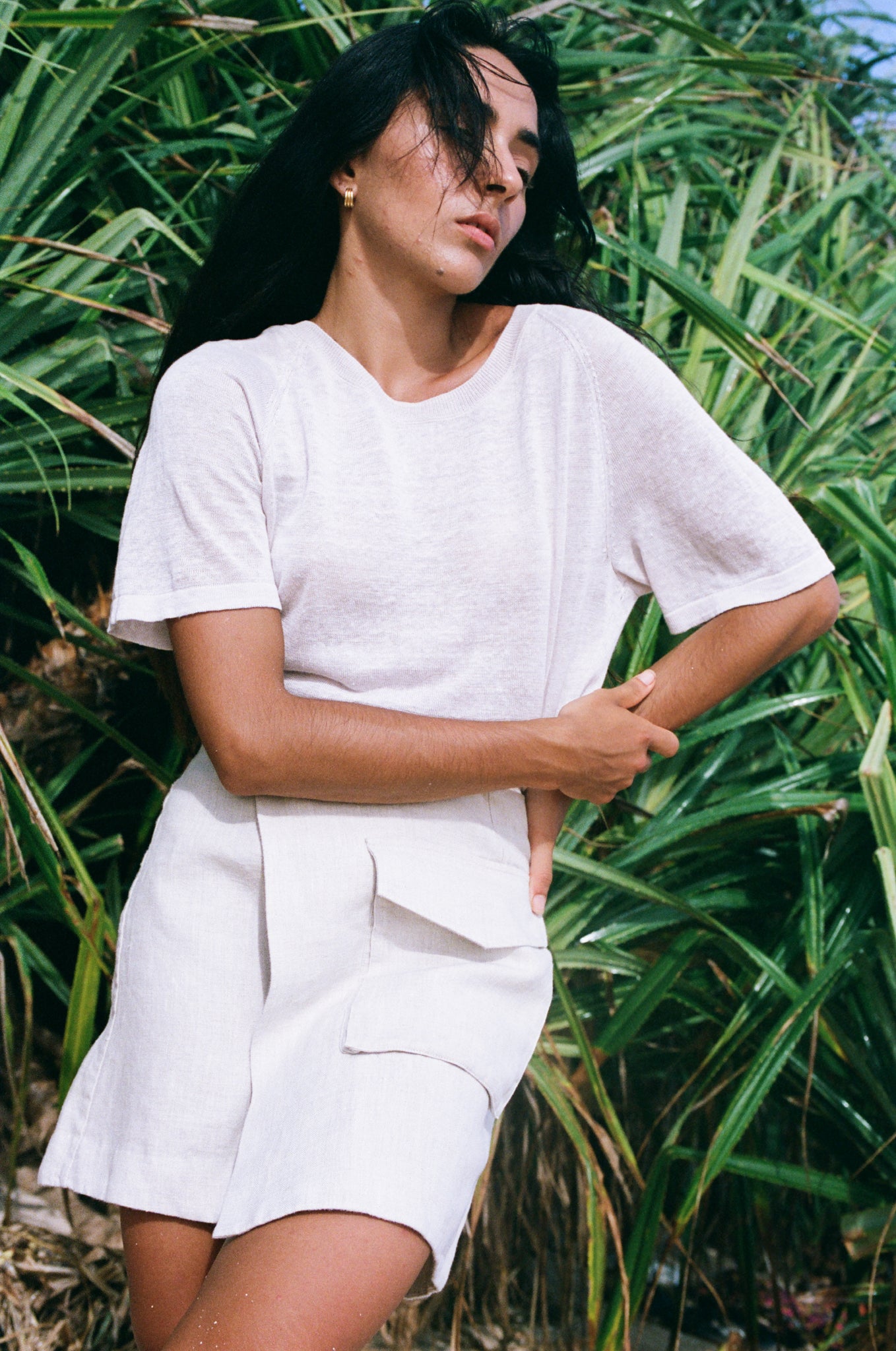 LILLY PILLY girl wearing Betty linen skirt and oatmeal Grace knit top standing in front of green foliage